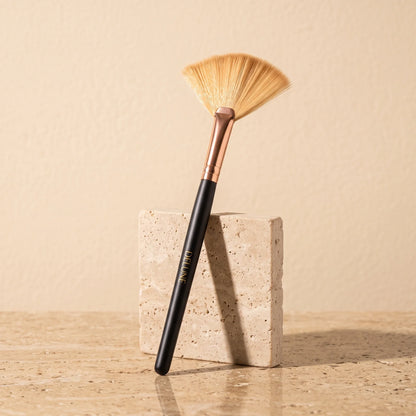 Delune clay mask fan brush with rose-gold ferrule leaning on a travertine block