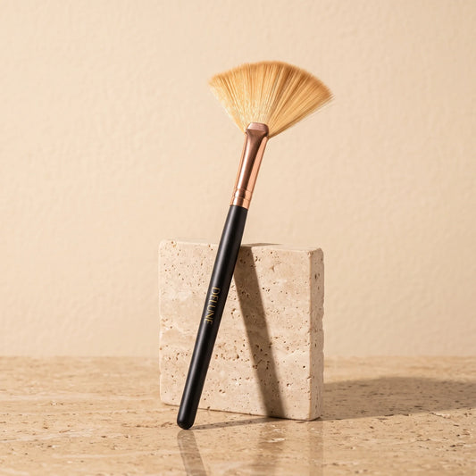 Delune clay mask fan brush with rose-gold ferrule leaning on a travertine block
