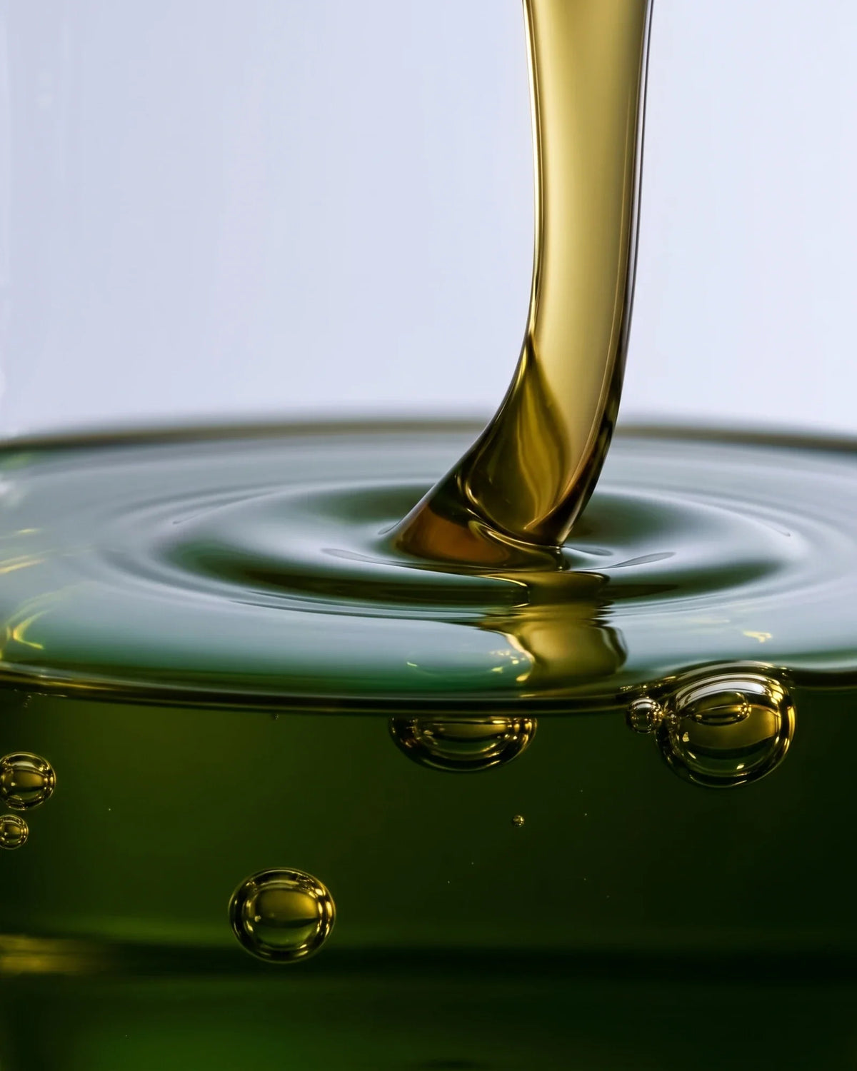 Clear 49% Tamanu Oil Serum texture: green-gold tamanu oil pouring into a pool with soft ripples